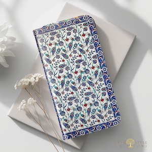 May include: A rectangular wallet featuring a white background with a dense pattern of blue and red tulips and green stems. The wallet has a wide blue border with a repeating floral motif and a silver zipper closure along the top edge.