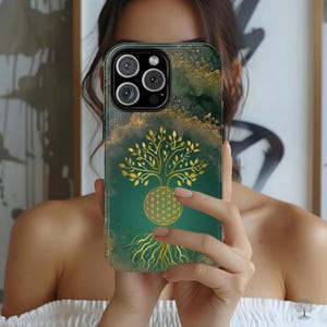 May include: A smartphone case featuring a deep emerald green background with gold-colored accents. The design displays a golden tree with a geometric flower of life pattern at its base, surrounded by gold-colored splatters and textures.