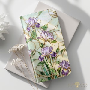 May include: A rectangular wallet featuring a stained glass pattern of purple iris flowers with green stems and leaves against a pale, iridescent background. The design includes dark outlines separating the floral and foliage segments.