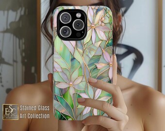 Può includere: Una custodia per telefono con un design floreale a vetrata. La custodia presenta un motivo di fiori verdi, bianchi e rosa con contorni color oro. Il testo "Art of Light & Nature" è scritto in alto. È visibile anche il testo "Stained Glass Art Collection".
