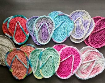 May include: A collection of multiple crochet flip-flop shaped scrubbers in various colors including pink, purple, blue, green, and beige. Each piece features a textured, circular base with a V-shaped strap detail, crafted from yarn.