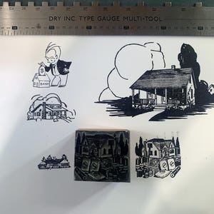 May include: Black and white illustrations of houses and a man depositing money into a bank. A wooden stamp with a house design is also present. A metal ruler with the text "DRY INC. TYPE GAUGE MULTI-TOOL" is at the top.