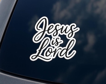Puede incluir: Una pegatina blanca con las palabras "Jesus is Lord" en una fuente cursiva. La pegatina tiene un contorno negro y está colocada sobre una superficie azul oscuro, posiblemente una ventana de coche.