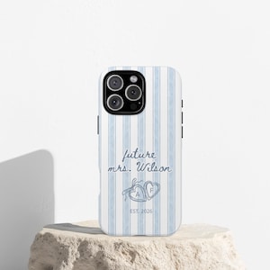 May include: A white and light blue striped phone case with the text "future mrs. Wilson" in a script font. Two heart-shaped designs with the letters "A" and "F" are below the text, with the year "EST. 2026" below the hearts.