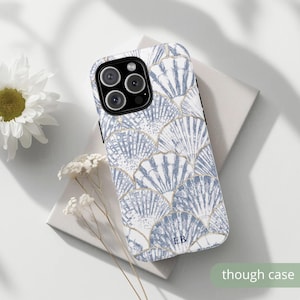 May include: A phone case with a seashell pattern in shades of blue and white, accented with gold outlines. The case has the initials "EB" and the text "though case". The case is on a white surface.