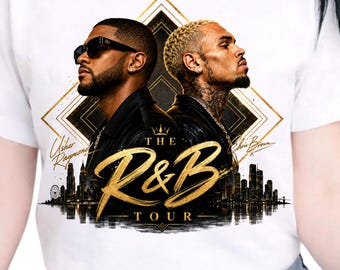 Peut inclure: Un t-shirt blanc avec une impression graphique représentant deux hommes dos à dos, dont l'un porte des lunettes de soleil. Le motif inclut un cadre doré en losange, une silhouette de ville et le texte doré "THE R&B TOUR" avec les noms Usher Raymond et Chris Brown.