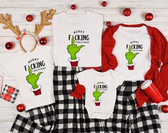 May include: White t-shirts, a onesie, and a red-sleeved shirt with the text "MERRY F*CKING CHRISTMAS" and a green hand giving the middle finger. Black and white plaid pajama pants are also visible, along with Christmas ornaments.