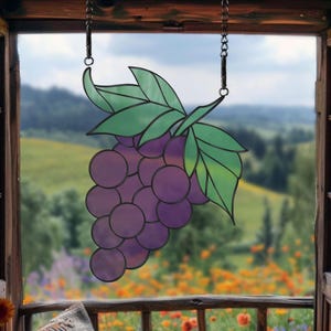 May include: A stained glass grape cluster hanging from a chain in a window. The grapes are purple and the leaves are green.