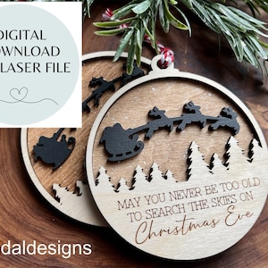 May include: A wooden Christmas ornament with a silhouette of Santa Claus and reindeer flying over a snowy forest. The ornament is engraved with the text "May you never be too old to search the skies on Christmas Eve."