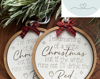 May include: Two round wooden Christmas ornaments with white centers and brown rims. The ornaments have the text "I'm dreaming of a white Christmas but if the white runs out I'll drink the Red". Each ornament has a red and black plaid bow.