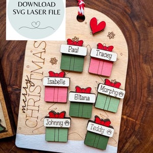 May include: A wooden arch-shaped Christmas ornament featuring the text "merry CHRISTMAS" and seven small gift-shaped wooden pieces attached, each personalized with names including Paul, Tracey, Isabelle, Elliana, Murphy, Johnny, and Teddy.