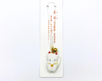 Op de afbeelding: Een witte vossenbedel met rode oren en gouden accenten, hangend aan een wit koord en een kleine gouden bel. De bedel is bevestigd aan een witte kaart met Japanse tekst.