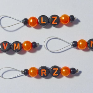 May include: Three orange and black beaded keychains with metal loops. Each keychain has a different name spelled out with black letter beads: LZ, VM, and RZ.