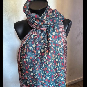 Può includere: Una sciarpa blu-verde con motivo paisley e accenti floreali rossi, bianchi e arancioni. La sciarpa è piegata e drappeggiata su un manichino.