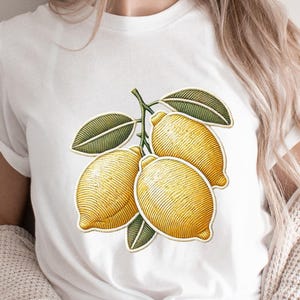 Pode incluir: Camiseta branca com um gráfico de três limões amarelos em um galho com folhas verdes.
