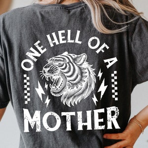 May include: A black t-shirt with a white graphic of a tiger with the text "One Hell of a Mother" printed on the back.