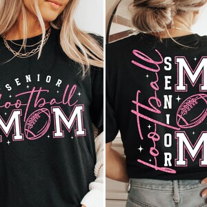 May include: Black t-shirt with the words "Senior Football Mom" in pink and white. The front of the shirt features a football graphic. The back of the shirt also has the words "Senior Football Mom" in pink.