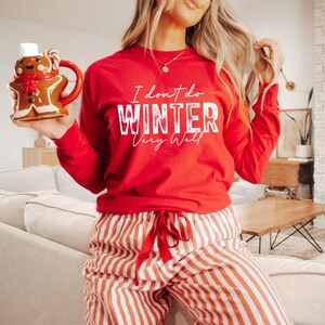 Puede incluir: Camiseta roja de manga larga con texto blanco que dice "No me gusta el invierno mucho". La camiseta se combina con pantalones de rayas rojas y blancas.