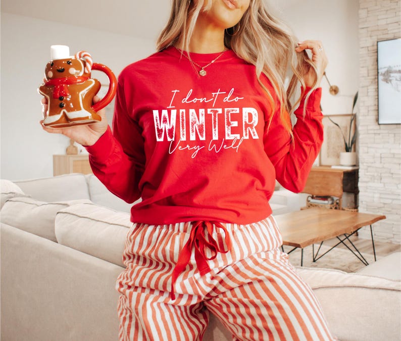 Puede incluir: Camiseta roja de manga larga con texto blanco que dice "No me gusta el invierno mucho". La camiseta se combina con pantalones de rayas rojas y blancas.
