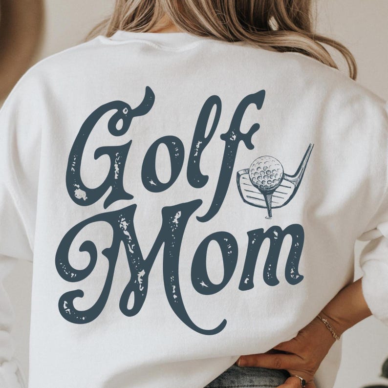 Pu&ograve; includere: Felpa bianca con una grafica blu che dice "Golf Mom" con una mazza da golf e una palla.