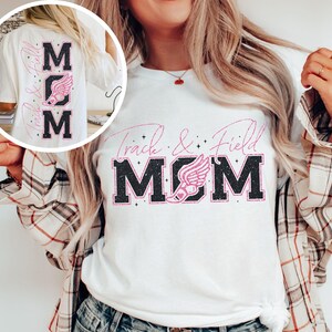 May include: White t-shirt with black text that says "Track & Field MOM" with a pink running shoe graphic. The shirt has a glittery effect.