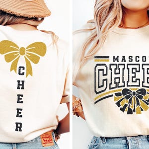 Puede incluir: Una camiseta blanca con un lazo de purpurina dorada y la palabra "CHEER" impresa verticalmente en la espalda. La parte delantera de la camiseta tiene un dise&ntilde;o de purpurina dorada con las palabras "MASCOT CHEER" impresas en negro.