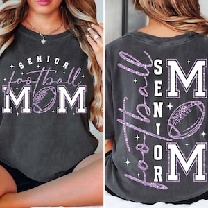 May include: Dark gray t-shirt with the words "SENIOR football MOM" in white and purple glitter. The front of the shirt features a football graphic. The back of the shirt has the words "Love the SENIOR football MOM" in purple glitter.