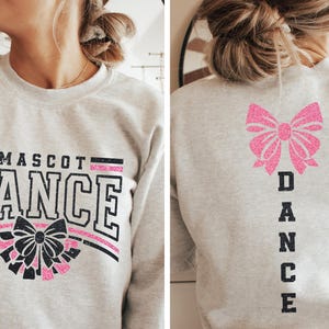 May include: A gray sweatshirt with the text "MASCOT DANCE" in black with a pink and black bow graphic on the front. The back of the sweatshirt has a pink bow graphic and the word "DANCE" vertically down the back.