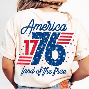 May include: A white t-shirt with a distressed blue and red graphic that says "America 1776 land of the free".