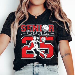 May include: Black t-shirt with red and white text that says "Senior twenty five" with a basketball player graphic.
