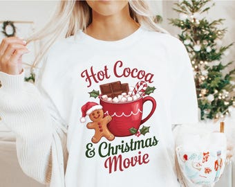 May include: White t-shirt with a festive graphic. The design features a red mug filled with marshmallows, chocolate, and a candy cane, with the text "Hot Cocoa & Christmas Movie." A gingerbread man wearing a Santa hat is also included.