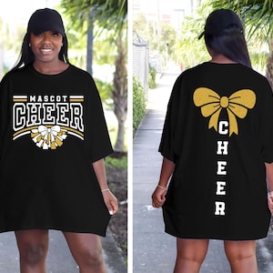 Puede incluir: Camiseta negra de gran tama&ntilde;o con letras doradas de purpurina que dicen "Mascot Cheer" en la parte delantera y "Cheer" verticalmente con un lazo dorado de purpurina en la parte posterior.