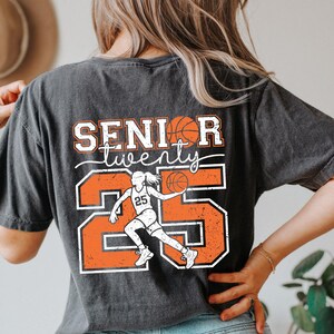 May include: Black t-shirt with a distressed orange and white graphic design. The graphic features a basketball player with the number 25 and the text "Senior twenty".
