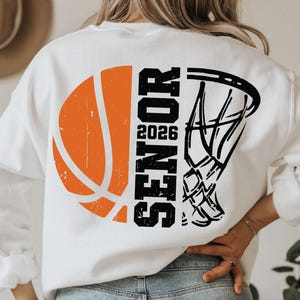 May include: White sweatshirt with a black and orange basketball graphic and the text "SENIOR 2026" on the back.
