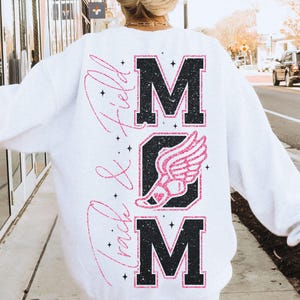 May include: White sweatshirt with a black and pink glitter design that says "MOM" with a pink running shoe and wings in the middle and "Track & Field" written vertically on the left side.
