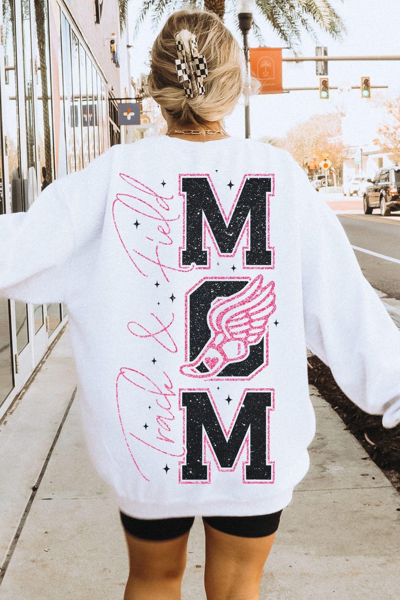 May include: White sweatshirt with a black and pink glitter design that says "MOM" with a pink running shoe and wings in the middle and "Track & Field" written vertically on the left side.