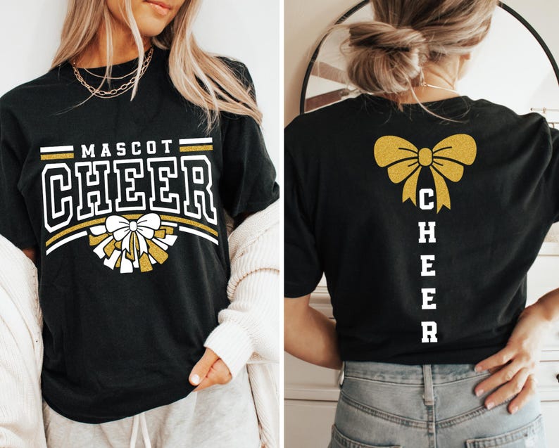 Puede incluir: Camiseta negra con texto en purpurina dorada que dice "MASCOT CHEER" y un lazo de purpurina dorada con pompones blancos. La parte posterior de la camiseta tiene un lazo de purpurina dorada y texto en purpurina blanca que dice "CHEER" verticalmente.