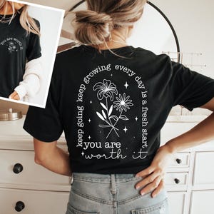 May include: Black t-shirt with white text and a floral design on the back. The text reads "keep going keep growing every day is a fresh start you are worth it".
