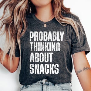 Könnte beinhalten: Ein graues T-Shirt mit dem Text "PROBABLY THINKING ABOUT SNACKS" in weiß gedruckt.