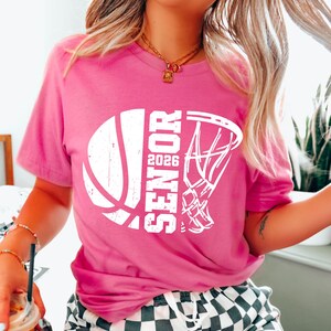 May include: Pink t-shirt with a white basketball and hoop graphic. The graphic says "Senior 2026".