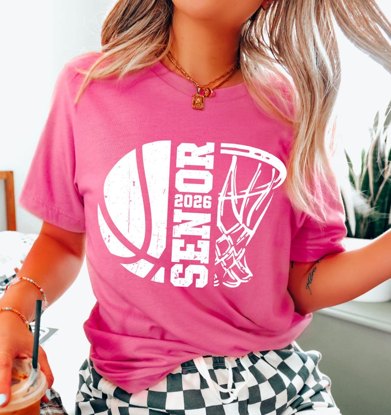 May include: Pink t-shirt with a white basketball and hoop graphic. The graphic says "Senior 2026".