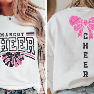Puede incluir: Camiseta blanca de manga larga con un lazo de purpurina rosa y el texto "CHEER" en la parte delantera. La parte posterior de la camiseta tiene un lazo de purpurina rosa y el texto "CHEER" verticalmente en la parte posterior.