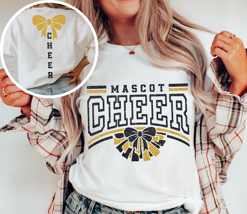 Puede incluir: Camiseta blanca con texto negro y dorado con purpurina que dice "MASCOT CHEER" con un lazo y pompones dorados con purpurina. La parte posterior de la camiseta tiene un lazo dorado con purpurina y la palabra "CHEER" verticalmente en la parte posterior.