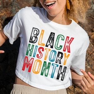 May include: A white cropped t-shirt with the text "BLACK HISTORY MONTH" printed in colorful, distressed letters.