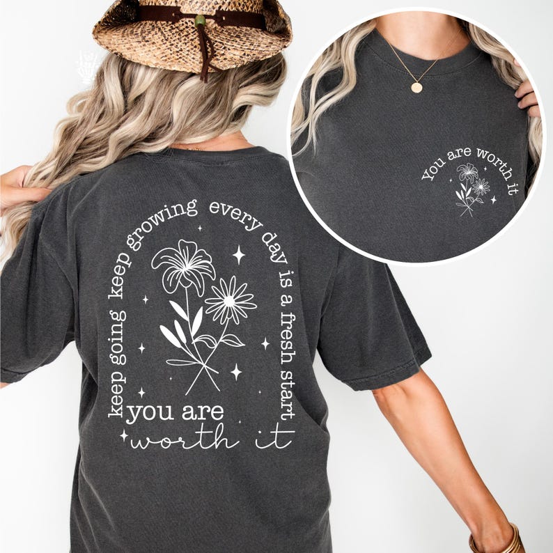 May include: A charcoal gray t-shirt with a white floral design and the text "keep going keep growing every day is a fresh start you are worth it" on the back. The front of the shirt has a smaller white floral design and the text "You are worth it".