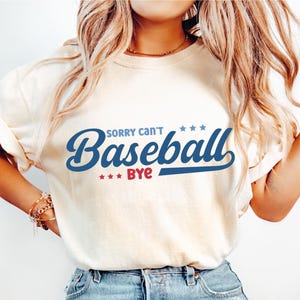 May include: A white t-shirt with the text "Sorry can't Baseball Bye" in blue and red lettering with stars.