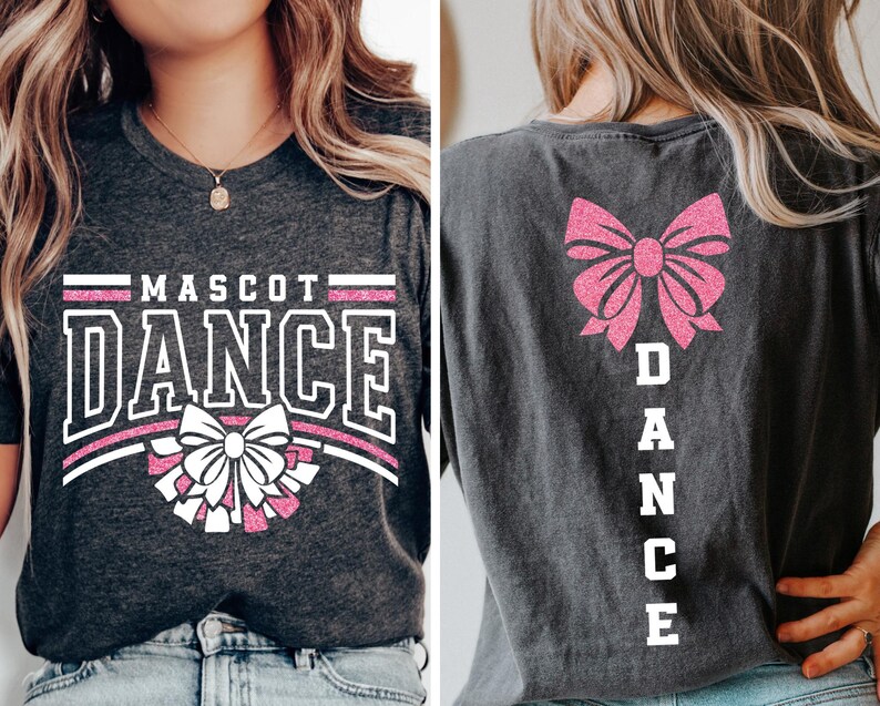 May include: A dark grey t-shirt with a white and pink glitter design. The front of the shirt says "MASCOT DANCE" with a pink bow and white pom-poms. The back of the shirt has a pink bow and the word "DANCE" spelled vertically in white.