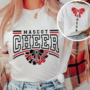 Puede incluir: Camiseta blanca con dise&ntilde;o de porrista negro y rojo. La parte delantera de la camiseta dice "Mascot Cheer" con un lazo rojo y pompones. La parte trasera de la camiseta dice "Cheer" verticalmente con un lazo rojo.