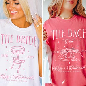 Pode incluir: Duas camisetas brancas com texto e gráficos rosa. A primeira camiseta diz "The Bride" com uma taça de champanhe rosa e o texto "ESTD 2025". A segunda camiseta diz "The Bach Club" com uma taça de champanhe rosa e o texto "ESTD 2025". Ambas as camisetas têm o texto "Betty's Bachelorette Palm Springs, California".