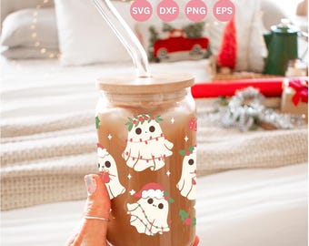 Könnte beinhalten: Ein durchsichtiges Glas im Dosen-Design mit einem Holzdeckel und einem Glasstrohhalm. Der Becher zeigt ein sich wiederholendes Muster von Cartoon-Geistern, die mit Lichterketten und Stechpalmen geschmückt sind. Der Text "16oz LIBBEY GLASS CAN WRAP" steht oben.